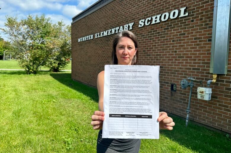 A woman stand in front of a school holding a petition.