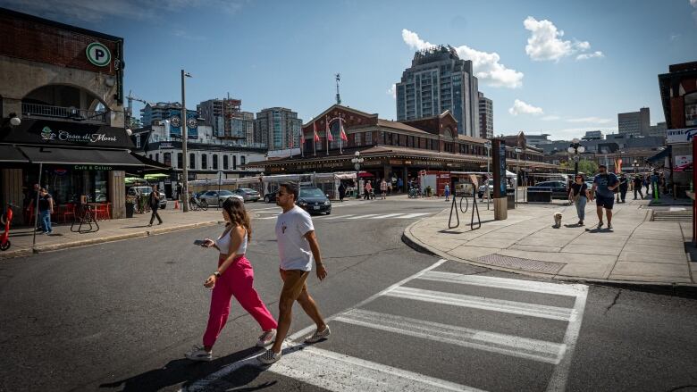 People cross a street in a historic city market area on a summer day.