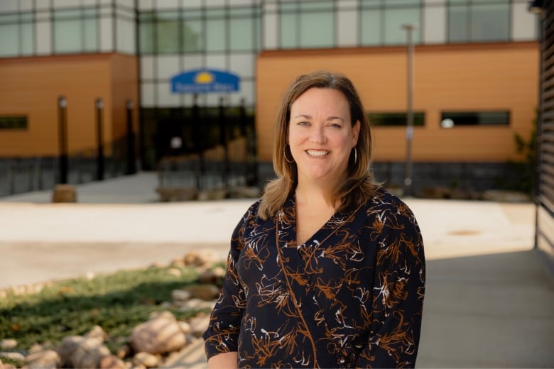 A woman stands in front of a university. She is smiling.