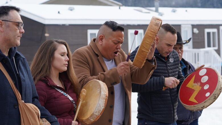 A line of people drumming and singing.