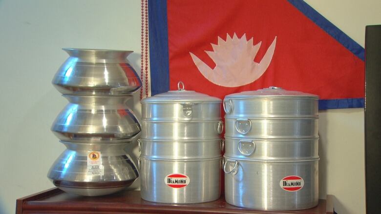 Pots and steamers are stacked above a shelf with half of the triangle of the Nepali flag visible