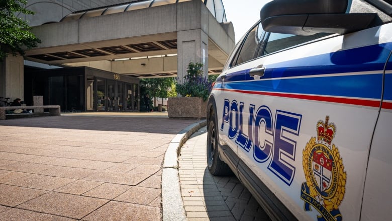 A white and blue police vehicle outside of a brown courthouse in summer.