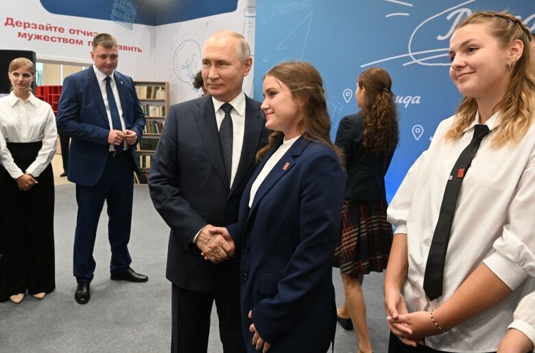 Russian President Vladimir Putin shakes hand with a teenager in a classroom.