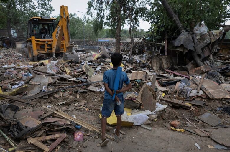 A young person stands beside a bulldozed home in a slum area.