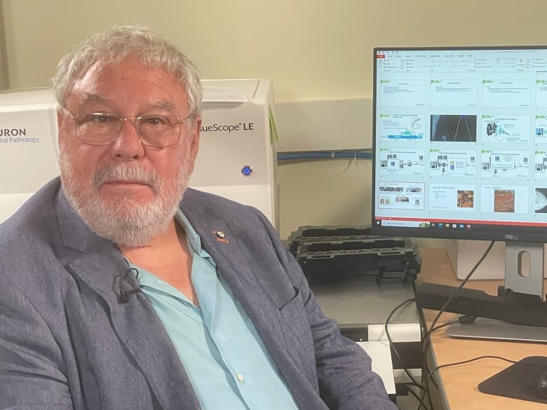 Man with white beard sitting in front of a computer screen.