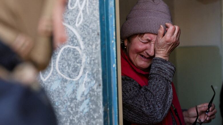 A woman in a wool coat holds her glasses and wipes her eyes as she cries 