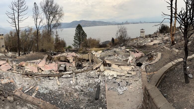 Charred remains of a home are visible with debris, with a lake on the horizon.