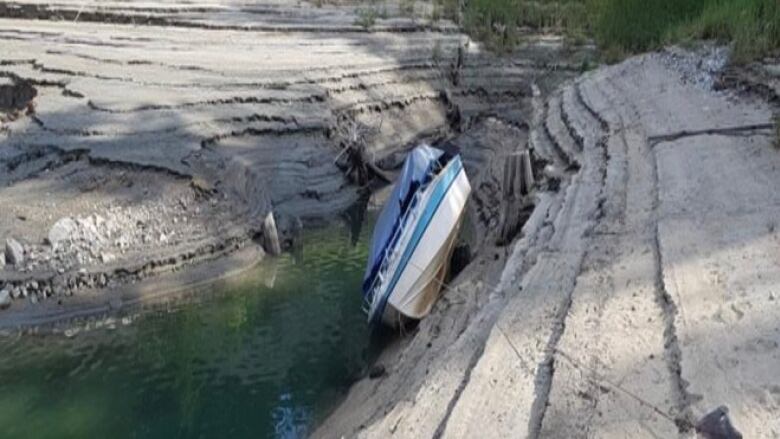 A boat hangs precariously on the side of a lake bottom that has been dry.