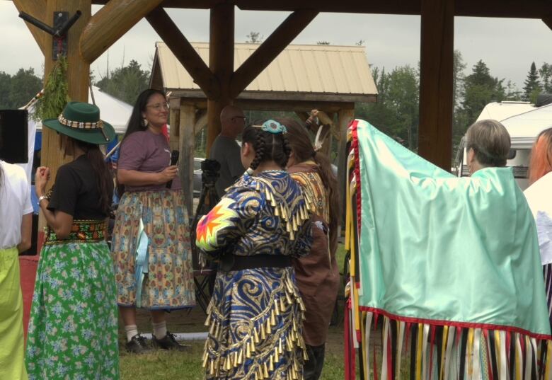 Women wearing long skirts gather outside near a gazebo.