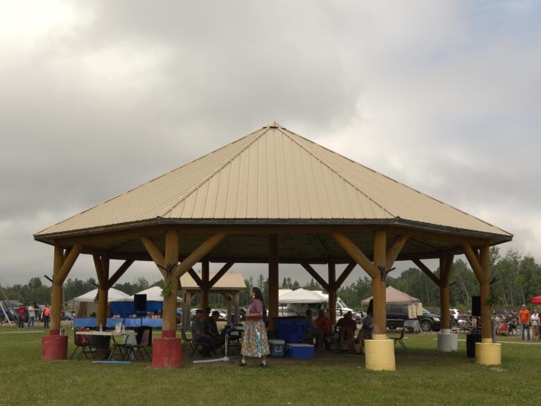 A woman wearing a purple shirt and long skirt stands outside underneath a gazebo.