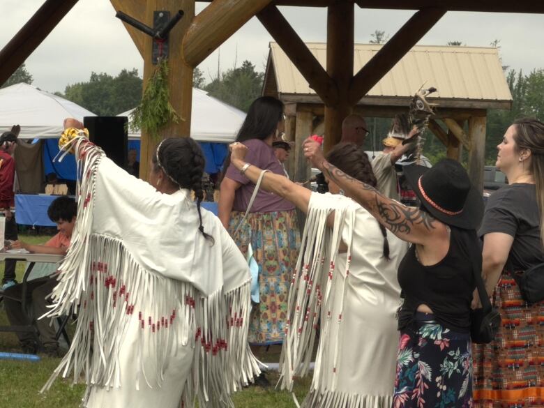 A group of women stand outside in front of a gazebo, each one raising their arm in a fist.