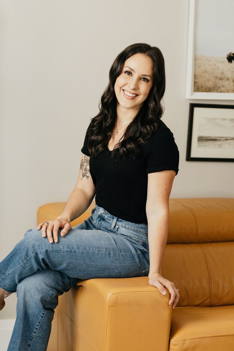 A woman siting on a sopha wearing a black top and jeans.