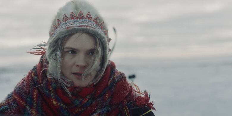 Still frame from the film The Tundra Within Me. Risten Anine Kvernmo Gaup stands in the icy tundra, staring, with snow in her hair.