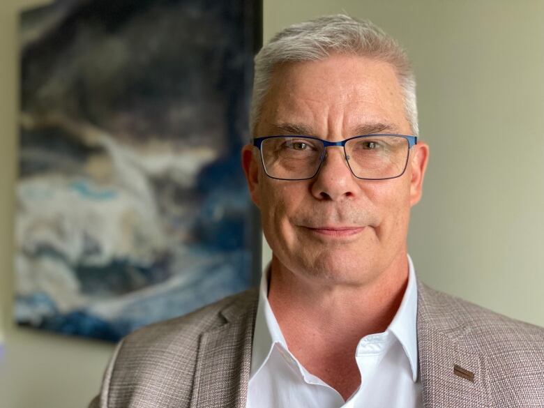 The photo shows a man wearing a business suit with glasses, looking directly into the camera.