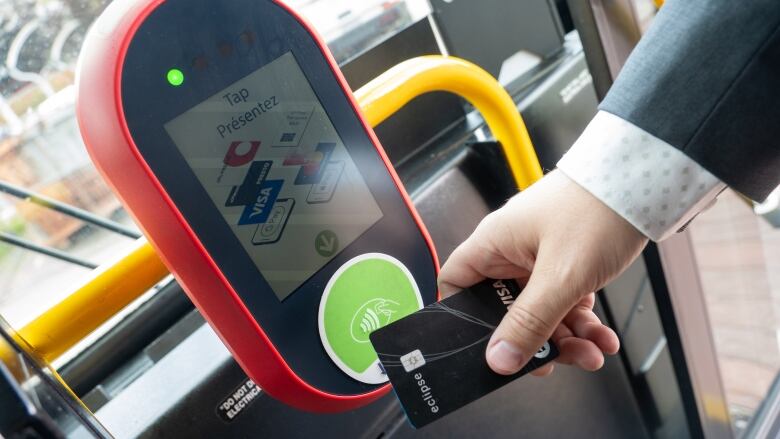 A person taps a credit card on a red pay station on a bus.