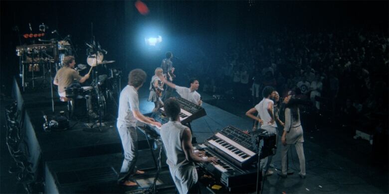 A group of musicians play their instruments in front of a large crowd. 