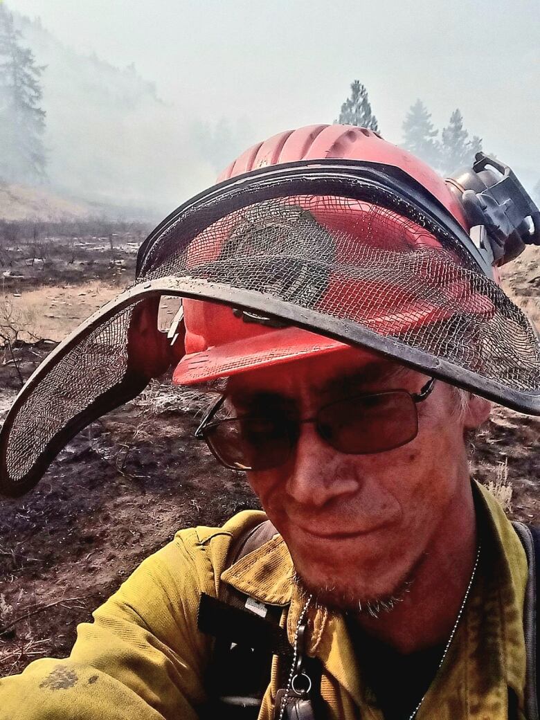 A firefighter in sunglasses and a sooty face looks is shown up close, wearing protective hard hat and a visor.