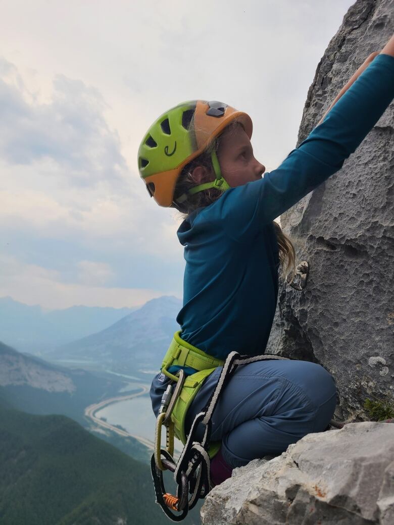 A child in a helmet and rock climbing gear is seen climbing on a mountain.