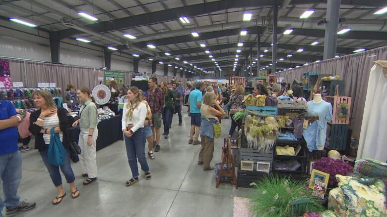 People walk next to tables with craft goods for sale.