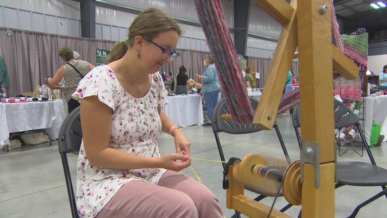 A woman spins yarn as she sits in a chair.