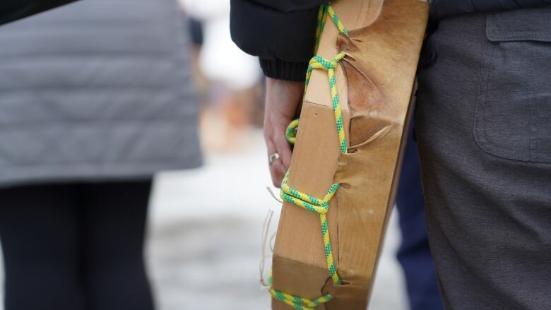 A person holds a ceremonial drum to their thigh.