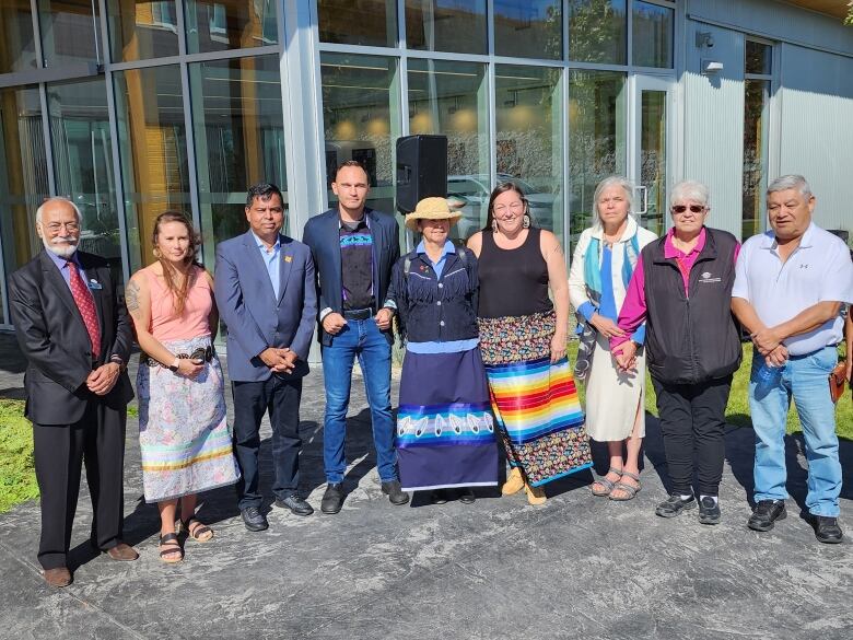 A lineup of people pose for a picture. Many of them are wearing Indigenous regalia.