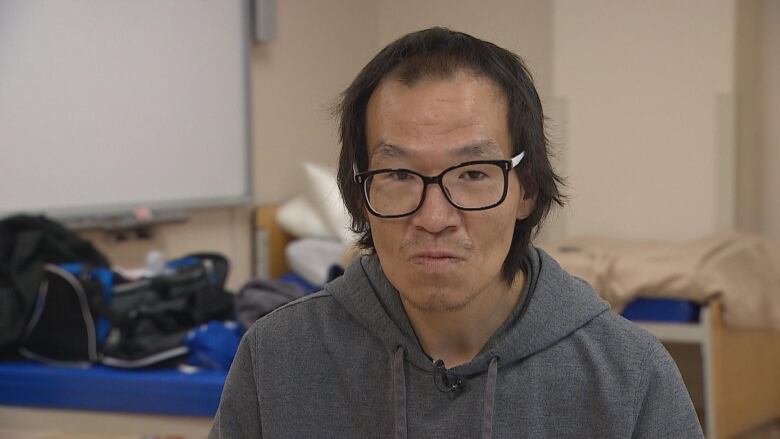 A man wearing glasses and a grey sweatshirt sits in a room.