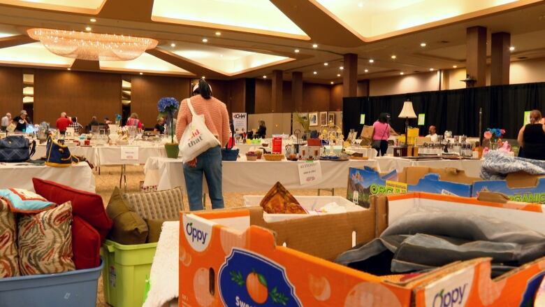 Tables in a large room are covered with various items, including books, toys and pillows.