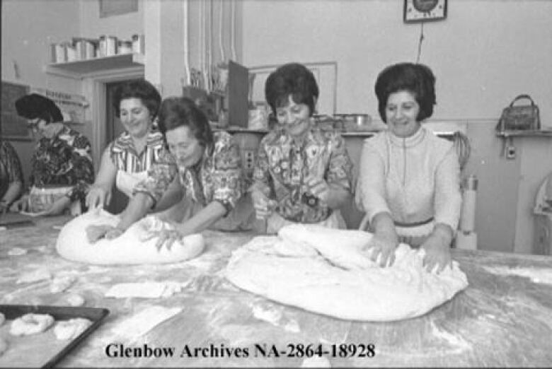 Four women knead bread dough on a table. 