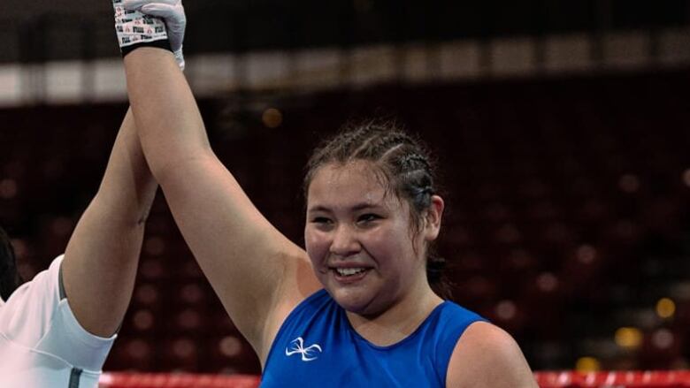 An Indigenous boxer in blue has her hand raised by the ref 