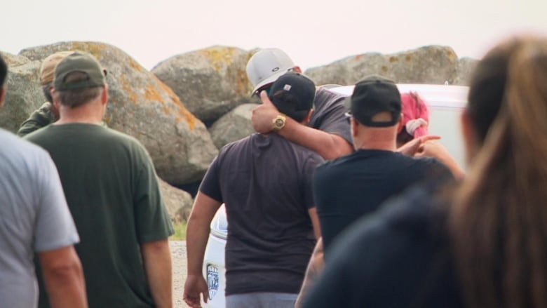 One man grabs another by the neck, in front of a group of onlookers.