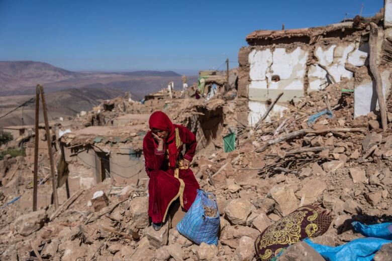 A woman sits amongst earthquake rubble.