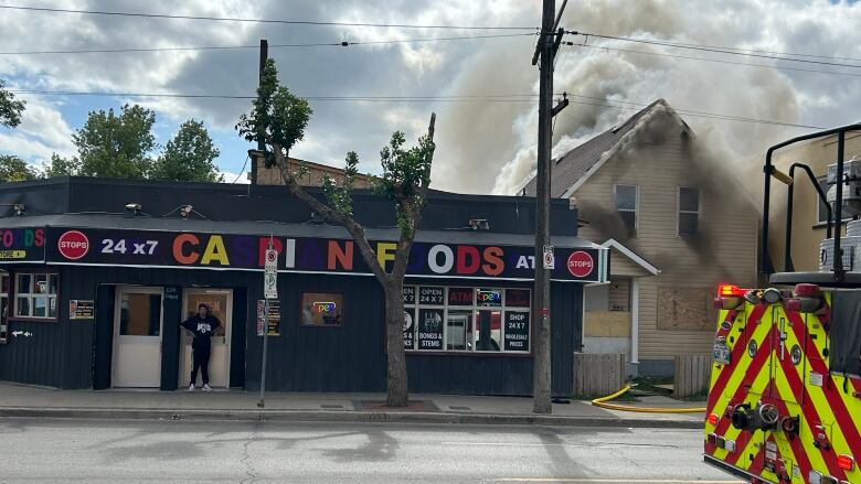 Plumes of smoke pour from a home on fire off a busy street.