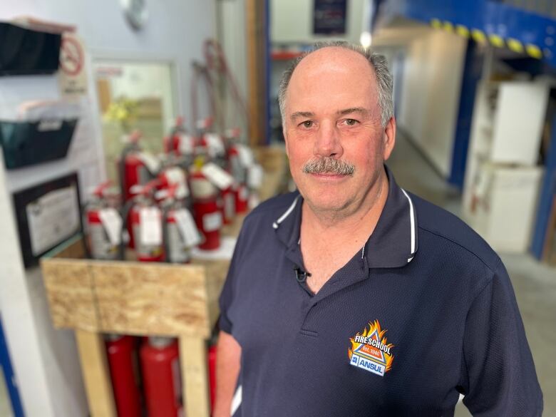 A man in a blue polo shirt stands in front of shelves of fire extinguishers