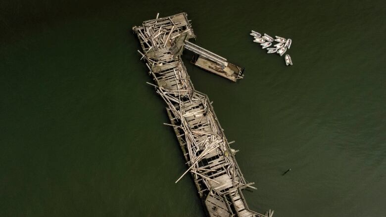 A long pier is pictured broken and battered from the air, with a collection of small boats to its right.