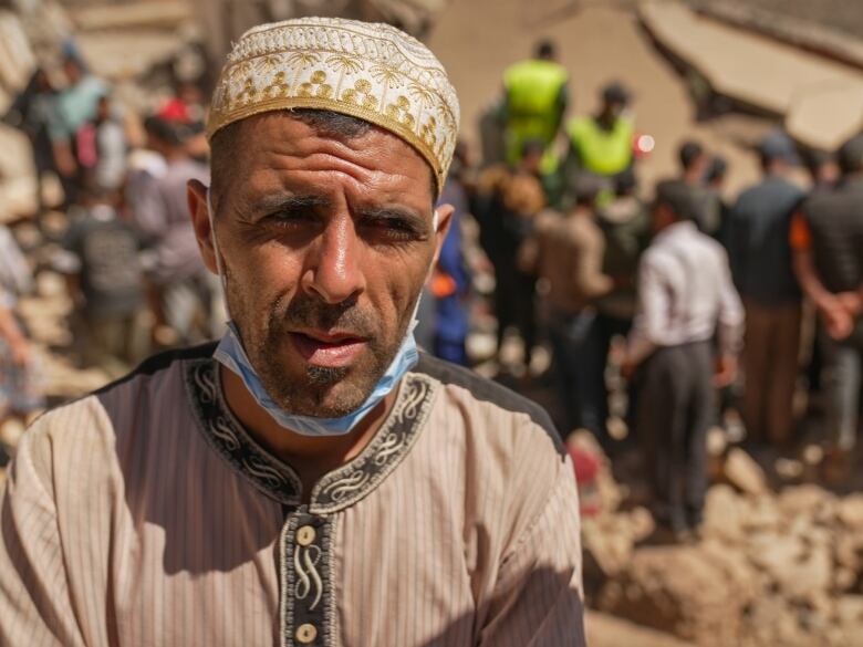 A middle-aged man stands squinting in front of the rubble of an earthquake.