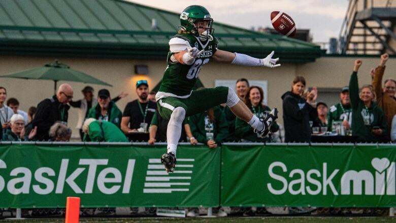 A football player in a green jersey jumps to catch a ball.