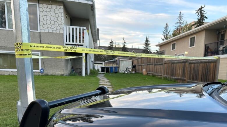 A police vehicle is parked outside a duplex, with police tape put up all around it.