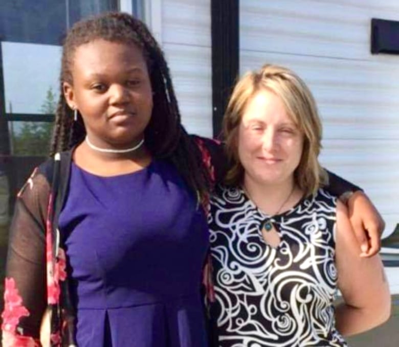 A young girl stands next to a woman, both smiling.