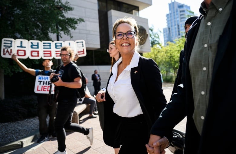 A woman walks toward a courthouse. People hold signs of support in the background including one saying 'FREEDOM.'