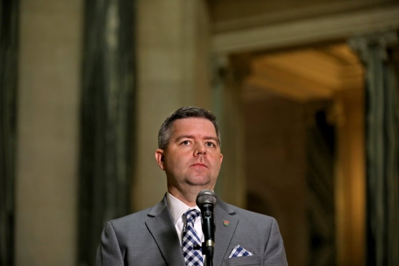 A man wearing a suit standing behind a mic. 