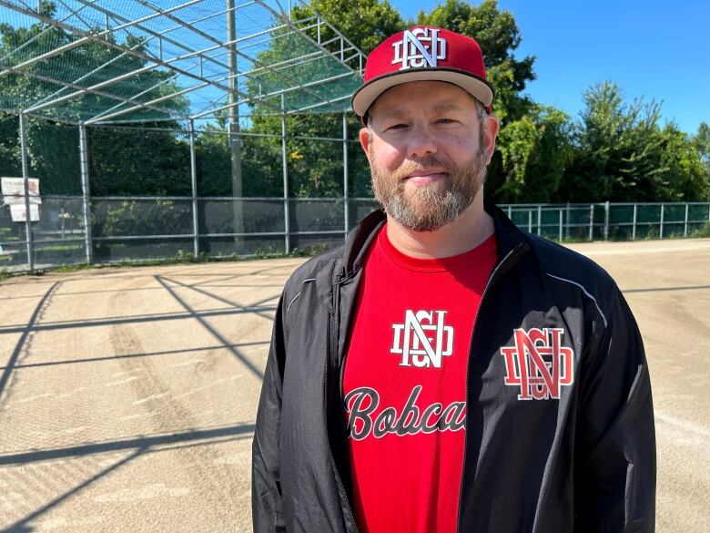 A man dressed in a red baseball jersey stands in the infield of a baseball diamond.