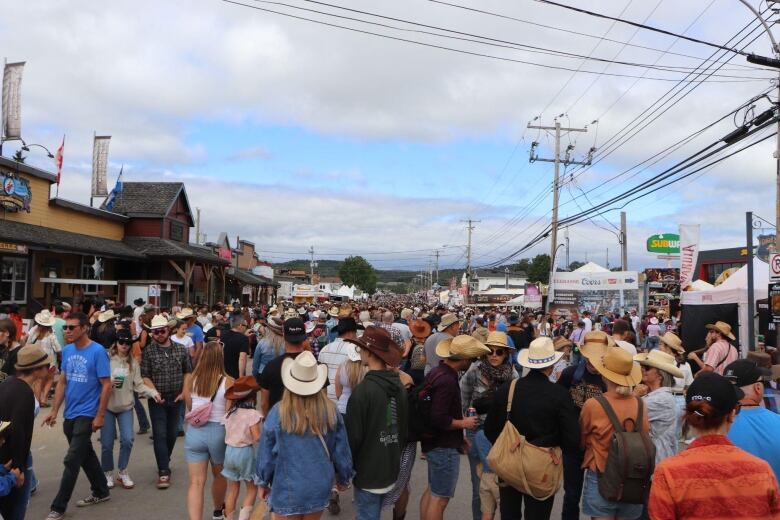 crowds of people pack onto a street wearing cowboy hats and western outfits