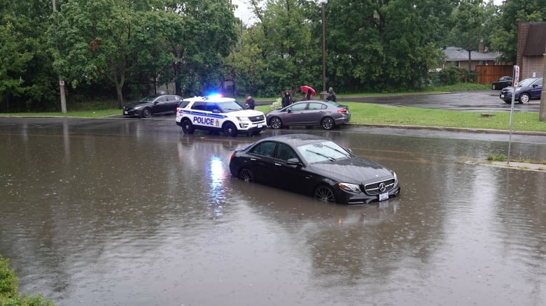 A car sits in a flooded street, with water midway up its wheels.  