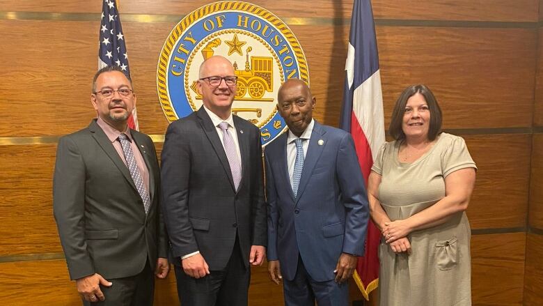 Four people are standing in front of a seal that says City of Houston, along with American and Texas flags.