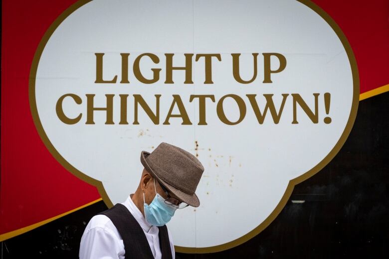 A man wearing a face mask walks past a sign that reads 'Light up Chinatown!'