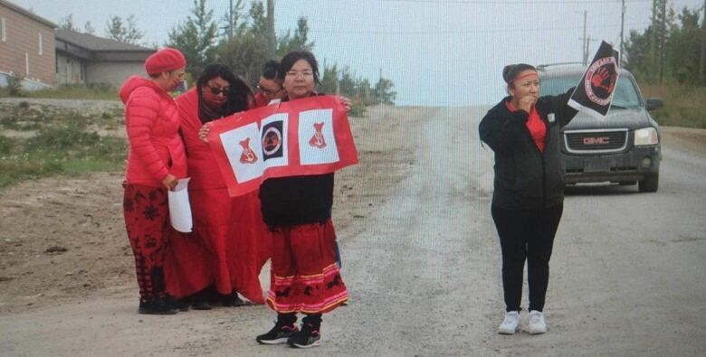 Six people dressed in red hold up signs with red and black icons in honour of missing and murdered Indigenous women and girls.