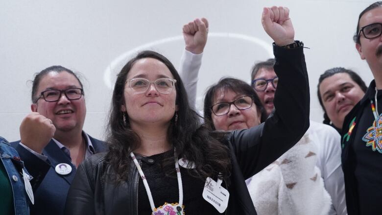 A woman raises her fist in the air. She's surrounded by members of her group that are smiling and making similar motions. 