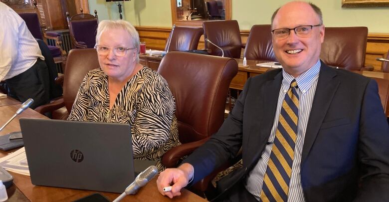 A woman and a man sit together at a desk in front of an open laptop.