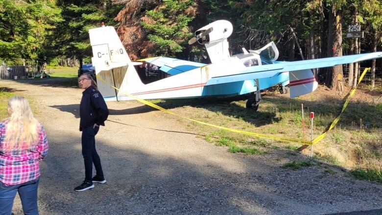 A small blue and white plane lies on a road, with two people standing nearby.